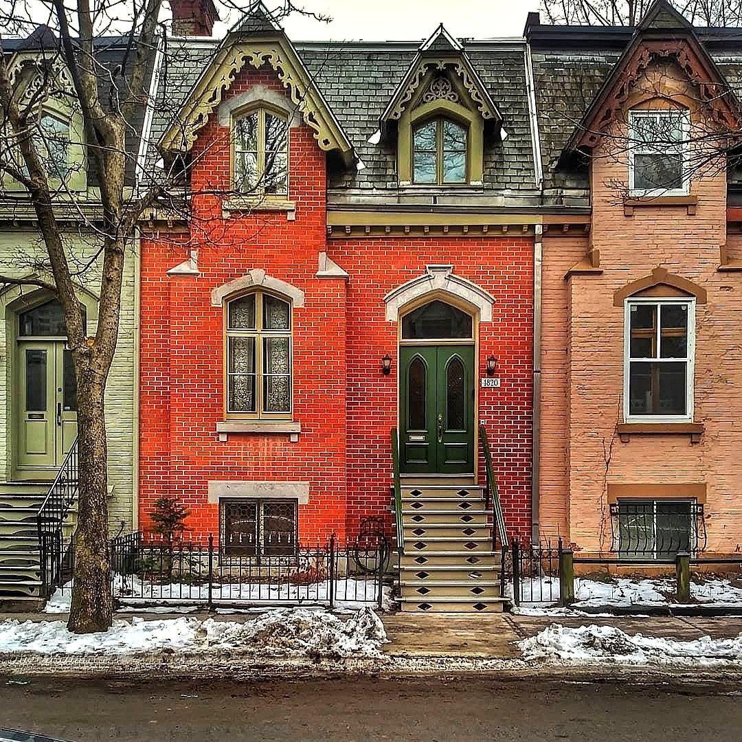 Three connected Victorian brick houses with pointed gables in red, yellow, and orange with snow on ground