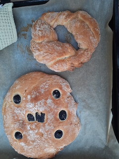 Top-down view of a round bread with olive decorations beside a croissant on baking paper