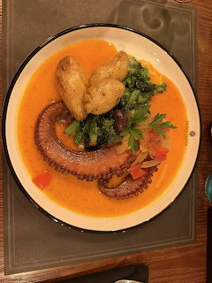 Top-down view of a seafood plate with octopus tentacle, broccoli, mushrooms, and orange sauce