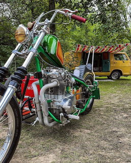 Custom green motorcycle with chrome engine parked outdoors near a yellow vintage camper van