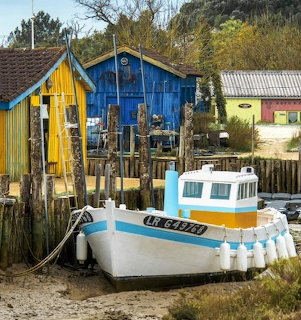 Fishing boat on sand near colorful blue and yellow harbor cabins at low tide