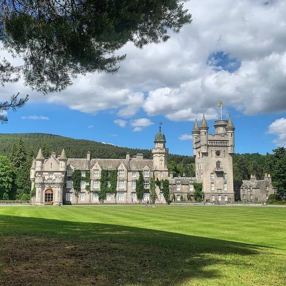 Balmoral Castle with towers on green lawn under cloudy blue sky