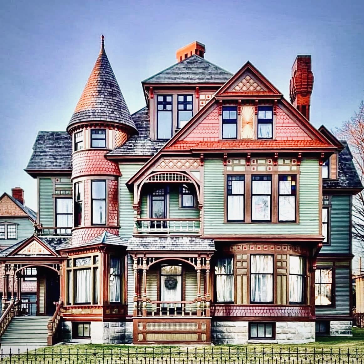 Victorian mansion with turrets, decorative woodwork, and wraparound porch against blue sky