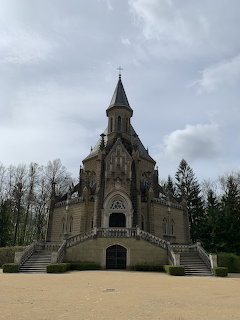 Gothic mausoleum with stairs and a tall central spire under a cloudy sky