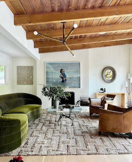 Mid-century modern living room with wood beam ceiling, green sofa, brown leather chair, and patterned rug