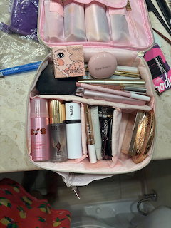 Open pink makeup organizer bag filled with various cosmetics, brushes, and skincare products