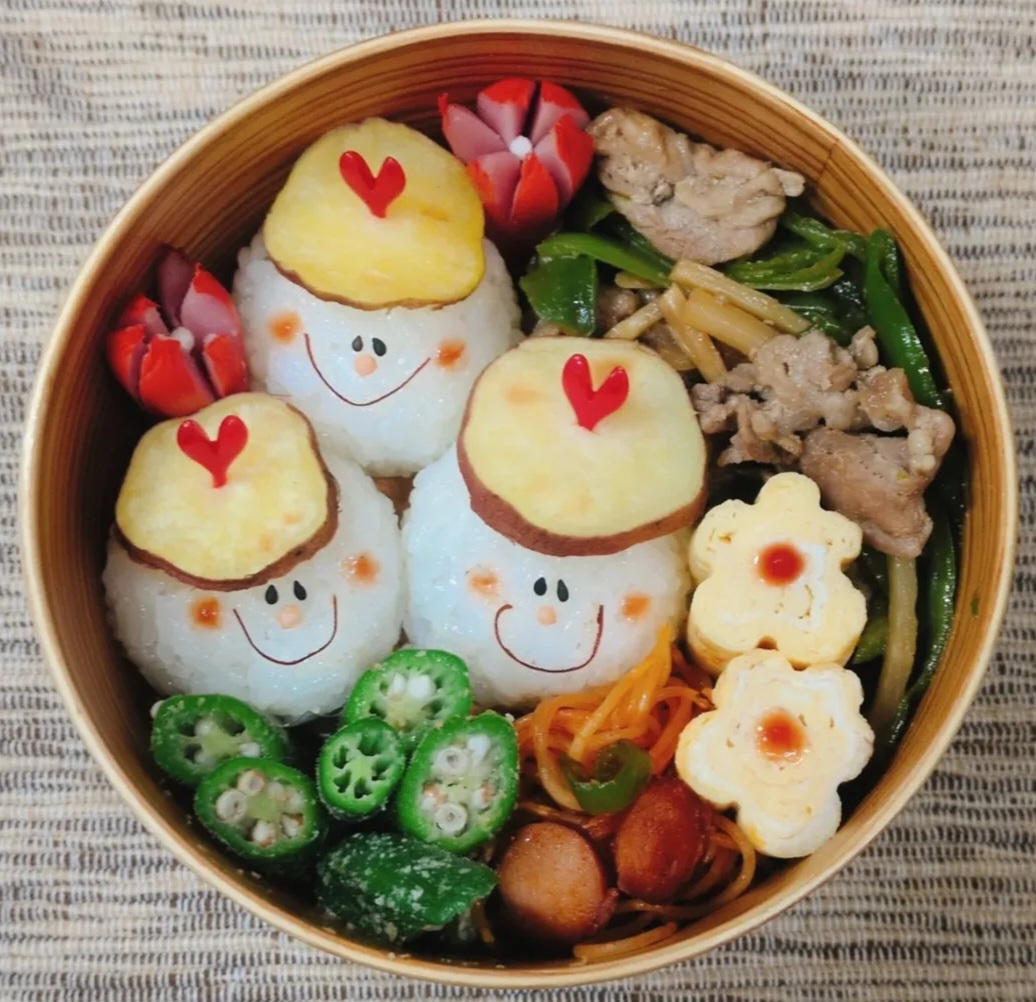 Cute bento lunch box with smiling rice balls, vegetables, meat, and flower-shaped slices