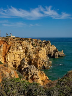 Rocky golden cliffs along a coastline with turquoise sea and a lighthouse in the distance