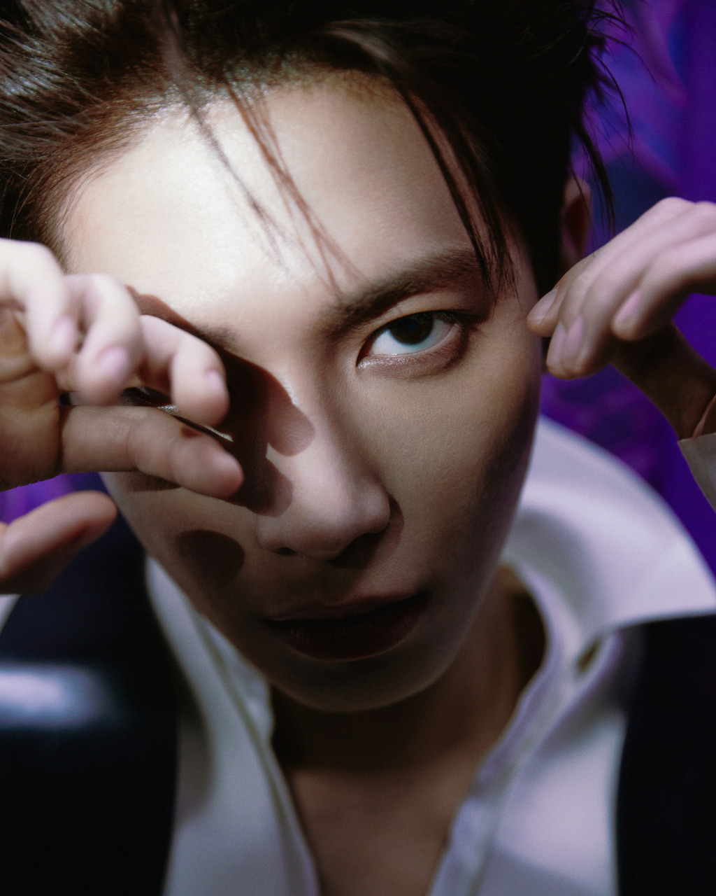 Young man with intense expression, hand raised near eye, purple background, dramatic lighting