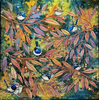 Colorful quilt with blue birds perched among pink and green leafy branches