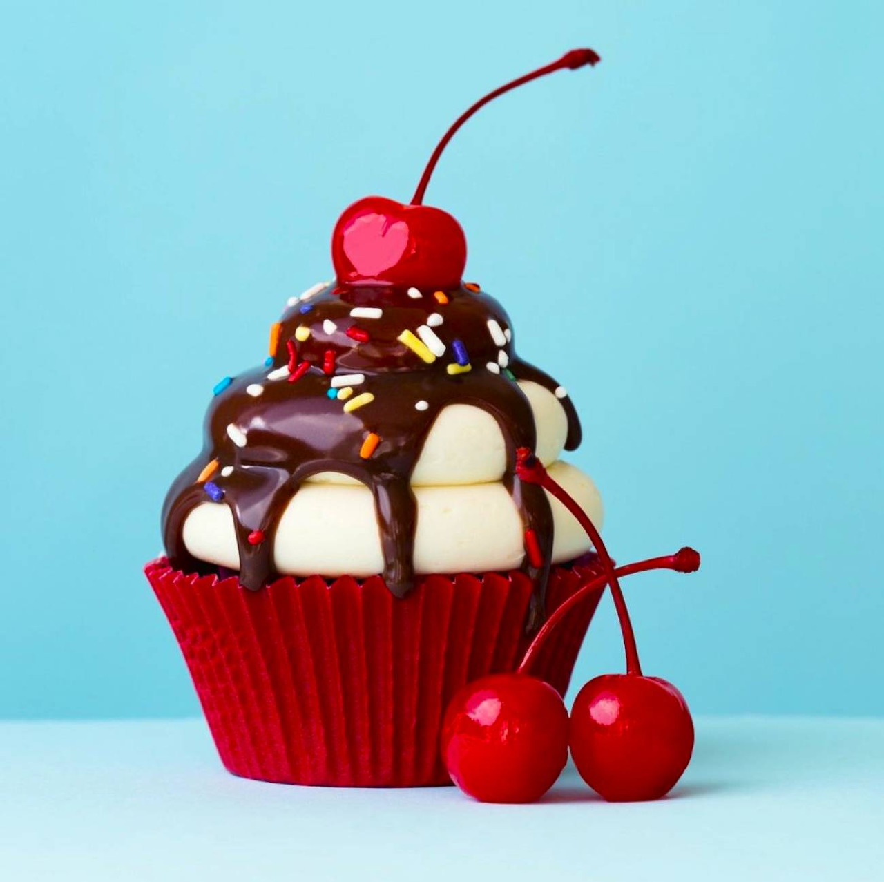 Chocolate-drizzled cupcake with sprinkles and cherries on a blue background