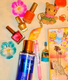 Flat lay of nail polish bottles, body mist spray, flower clips, bear keychain, and tropical postcard