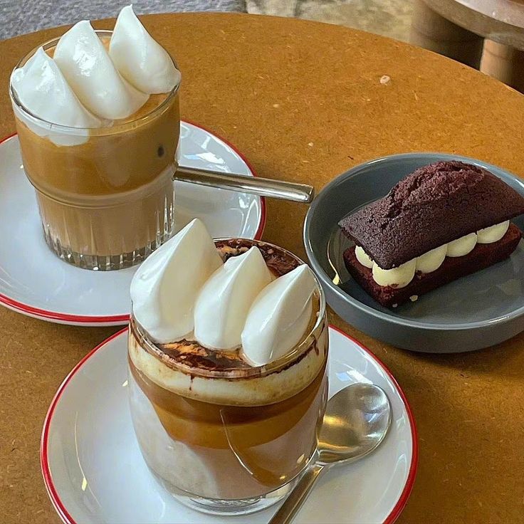 Two creamy coffee drinks with whipped cream and a chocolate brownie on a wooden table