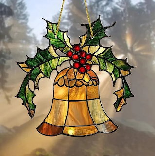 Stained glass ornament of two golden bells decorated with green holly leaves and red berries hanging in a window