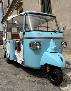 Turquoise vintage Piaggio Ape Calessino three-wheeler parked on cobblestone street in Italy