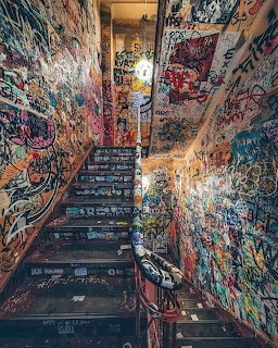 Indoor staircase densely covered in colorful graffiti and street art with light from above