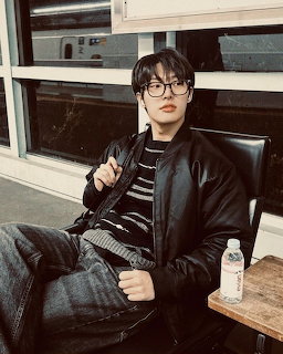 Young man with glasses sitting in a chair wearing a black leather jacket and striped sweater