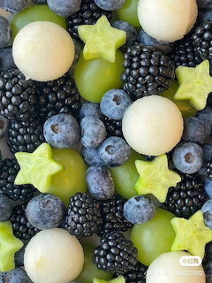 Overhead view of mixed fresh fruits including blackberries, blueberries, starfruit, melon balls, and grapes