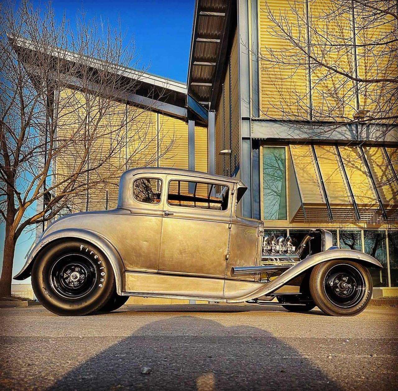 Beige 1930s Ford Model A coupe parked outside yellow building