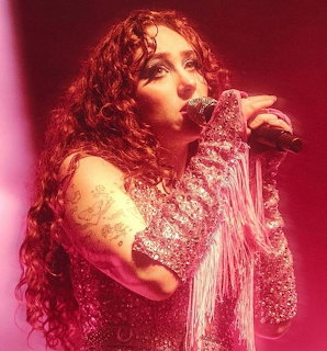 Chappell Roan singing into a microphone on stage in a glittery fringed outfit
