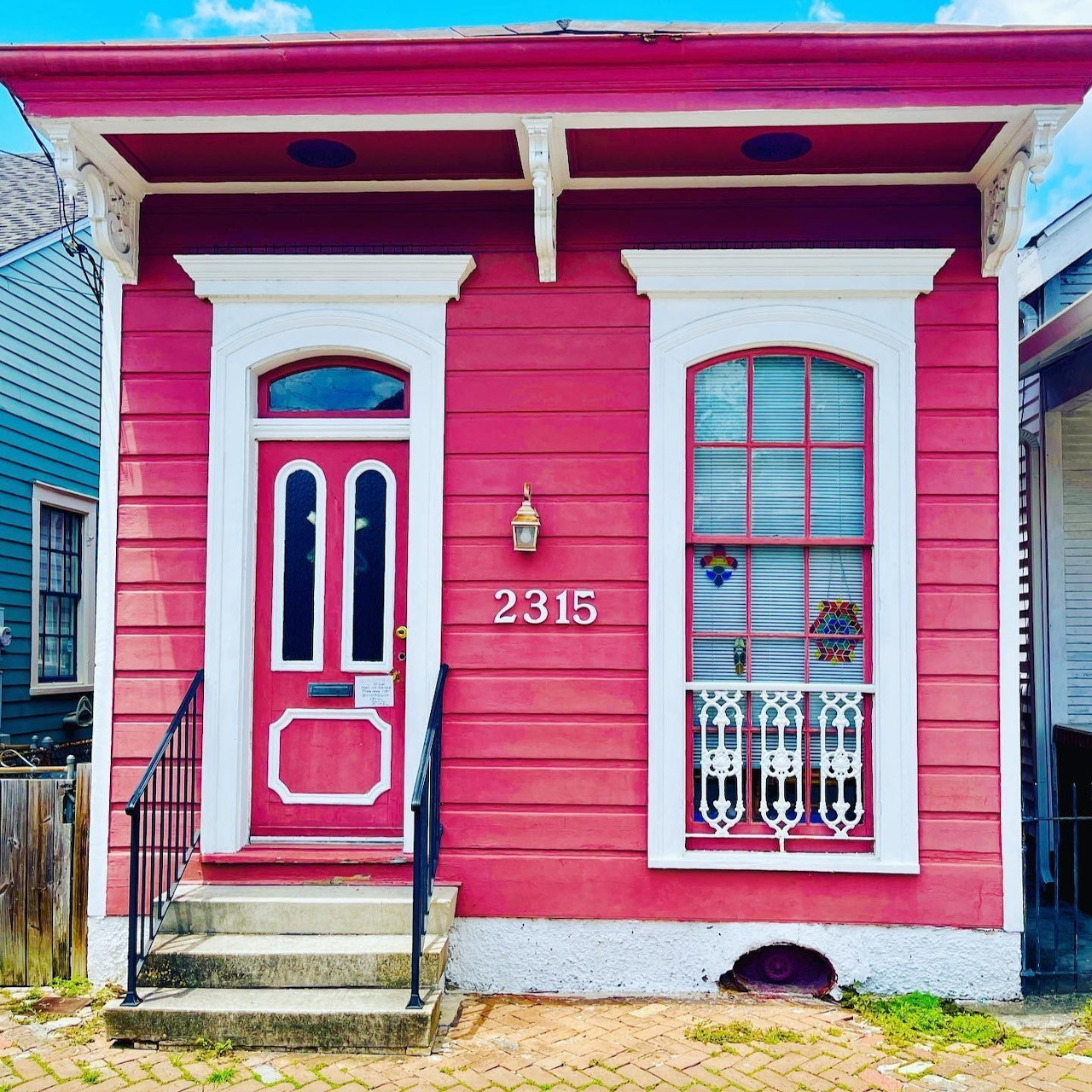 Vibrant pink tiny house with white columns, red door, and arched window displaying address 2315