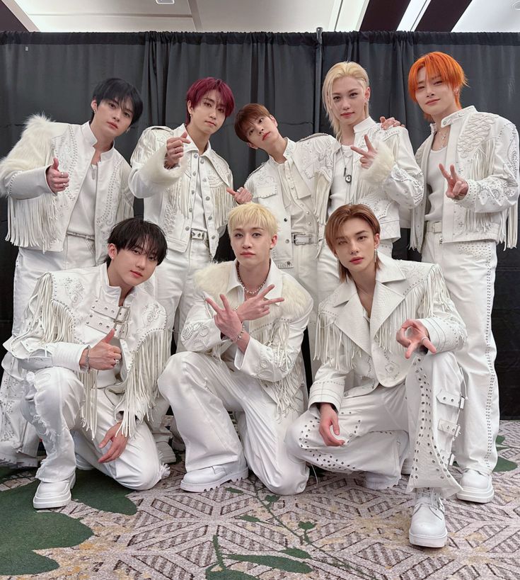Eight men in white outfits posing together making hand gestures