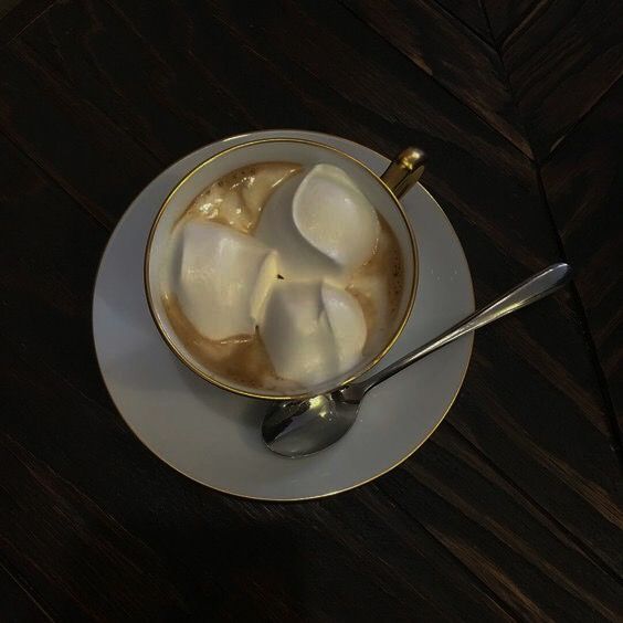 Top view of creamy coffee in a white cup and saucer with a spoon on a dark wooden table