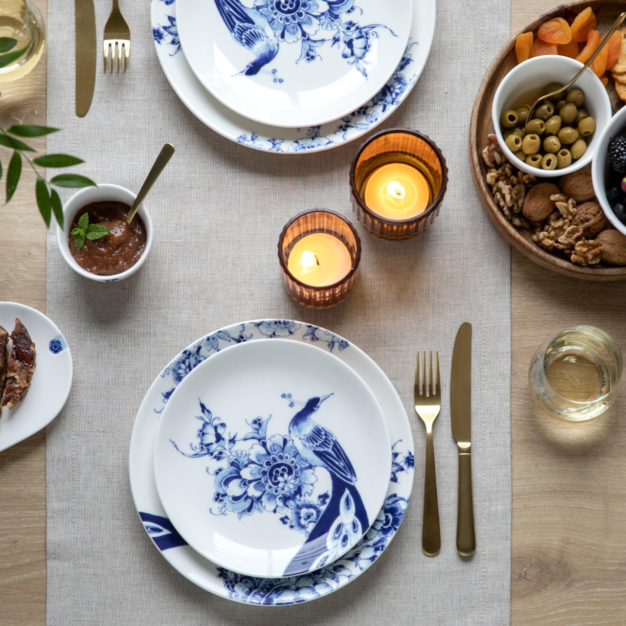 Elegant dinner table with blue floral porcelain plates, candles, wine glasses, and appetizer bowls on linen tablecloth