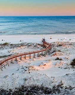 Wooden boardwalk crossing sandy dunes to a calm beach and ocean at sunset