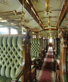 Luxurious vintage train car interior with green tufted seats and ornate wood details