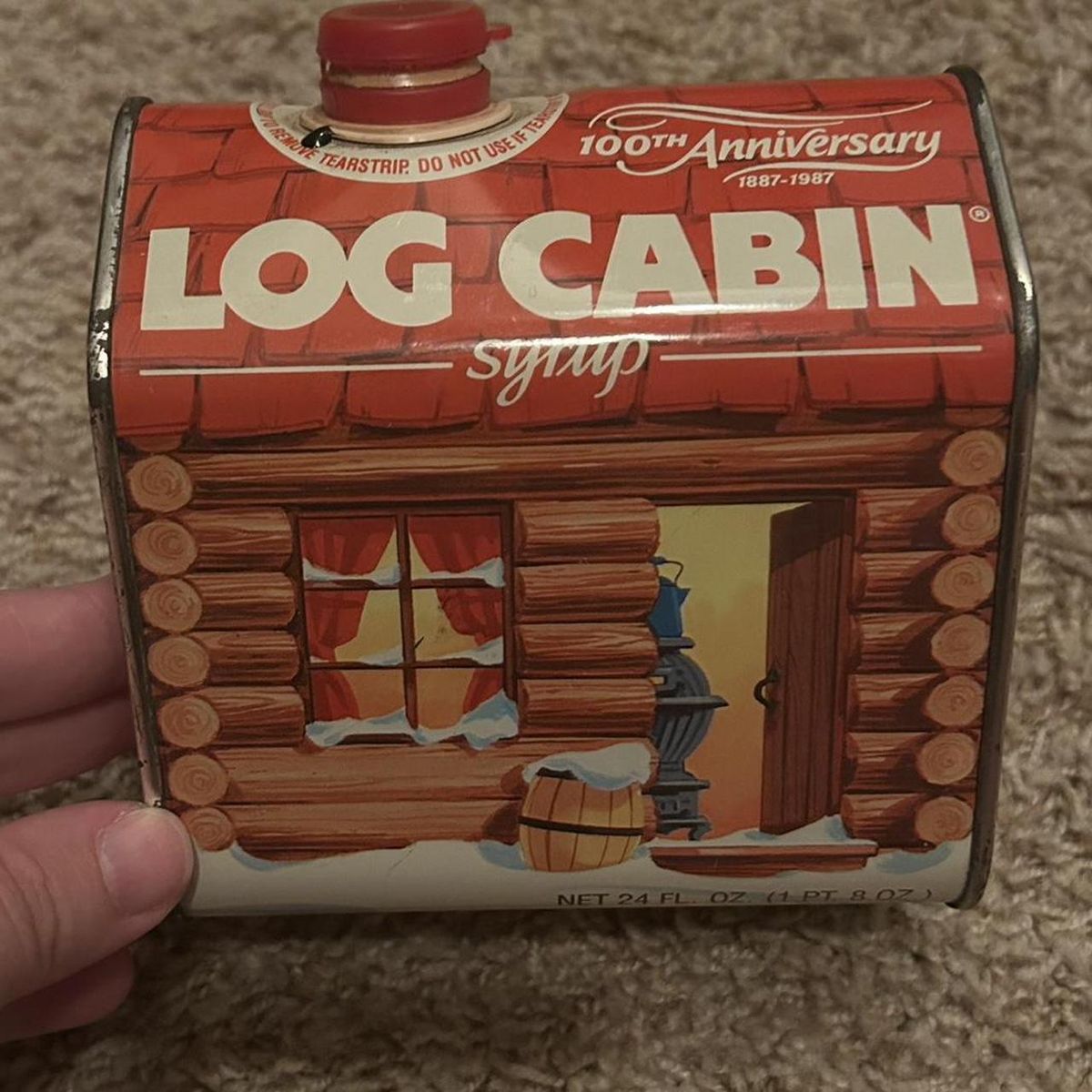 Hand holding a vintage Log Cabin syrup can shaped like a small log cabin
