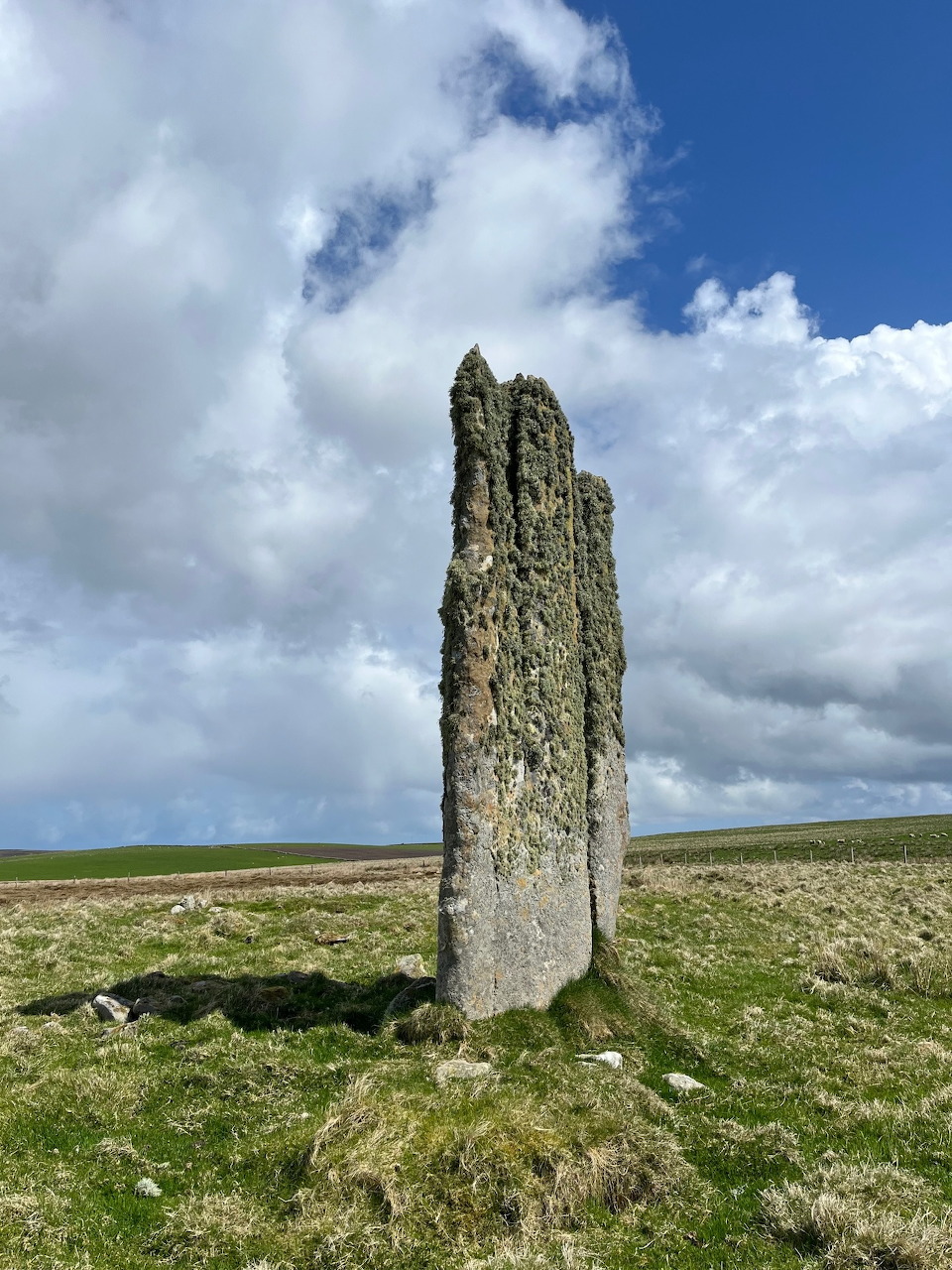 Tall weathered standing stone in open moorland under cloudy blue sky