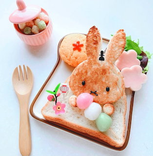 Bunny-shaped pastry on toast with pastel sweets, a wooden fork, and a small dessert cup