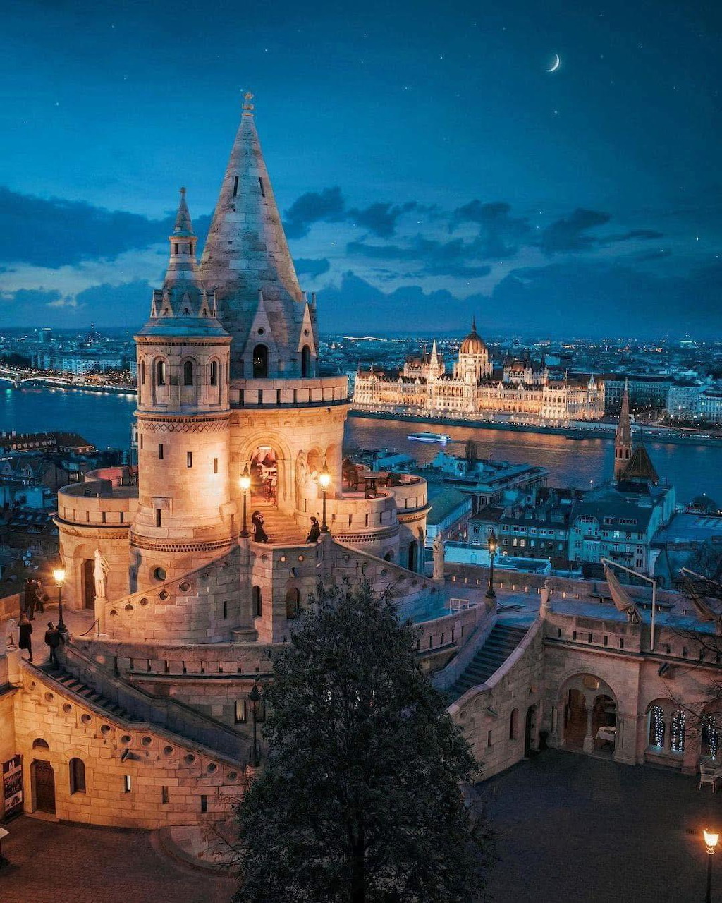 Illuminated Fisherman's Bastion towers in Budapest at dusk with river and city view