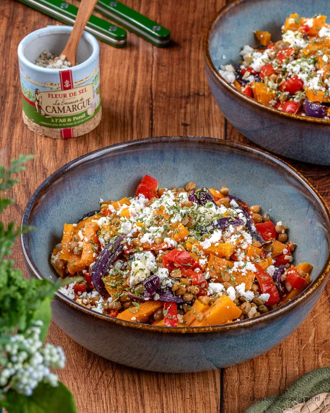 Two bowls of lentil salad with sweet potato, feta, and vegetables on a wooden table