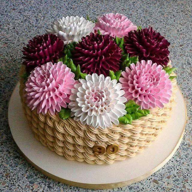 Round cake decorated with pink, burgundy and white buttercream dahlia flowers on basket-weave frosting