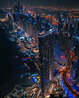 Aerial night view of illuminated Address Beach Resort tower in Dubai with glowing city lights and coastal roads