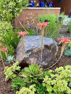 Large rock centerpiece in garden bed with colorful succulents and flowering plants