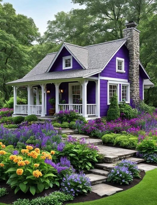 Purple cottage with white columns and porch, framed by lush gardens with purple and yellow flowers