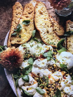 Grilled bread slices with burrata cheese, herbs, and decorative flowers on dark platter