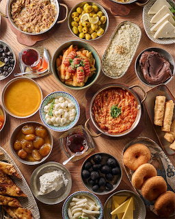 Overhead view of a table with many Mediterranean dishes, olives, dips, rice, stuffed peppers, and bread