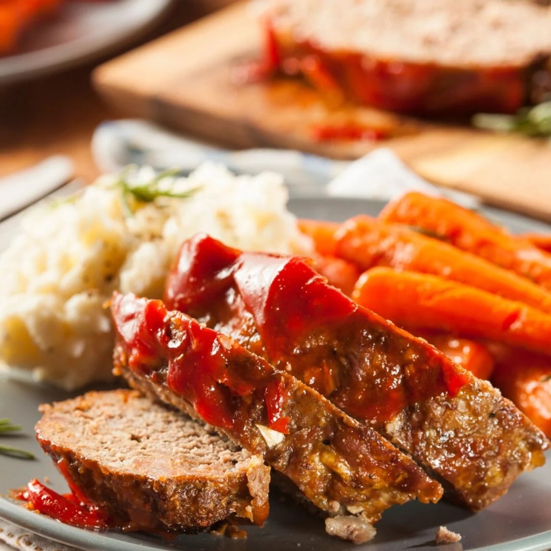 Sliced meatloaf with glazed carrots and mashed potatoes on a plate