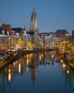 Historic Dutch canal at dusk with lit buildings and church spire reflecting in water
