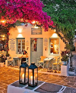 Greek cafe bar with pink bougainvillea, warm evening lighting, outdoor tables, and candle lanterns in Karpathos