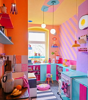 Brightly colored kitchen with orange walls, pink and turquoise cabinets, striped purple ceiling, and colorful pendant lights