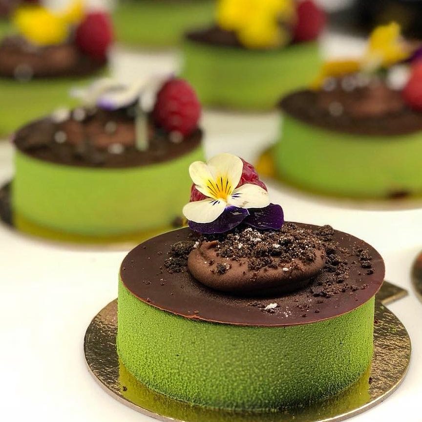 Round green matcha cakes with chocolate tops and flower garnishes on gold bases