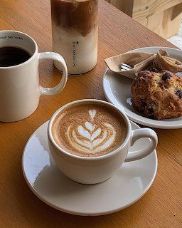 Latte with heart foam art, black coffee, iced coffee, and blueberry muffin on wooden table