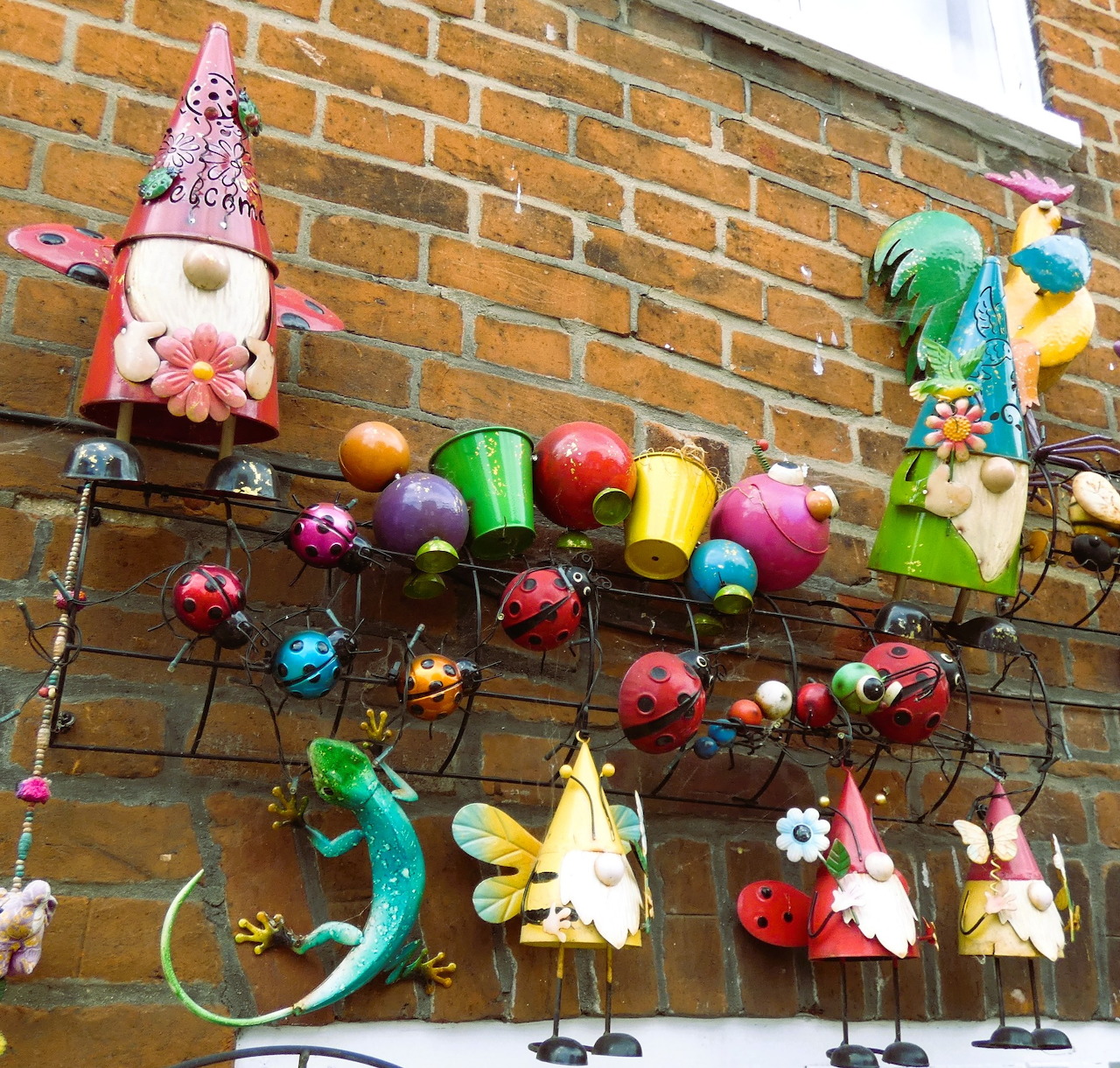 Colorful garden gnomes and ladybug ornaments hanging on brick wall with decorative bugs and flowers