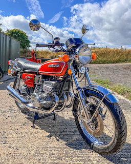 Red and blue Suzuki GT550 motorcycle on gravel with field background