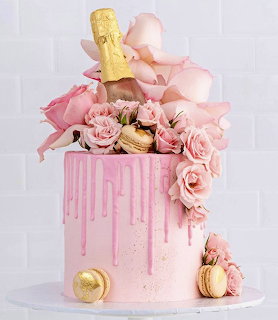 Pink drip cake with roses, macarons, and a champagne bottle topper